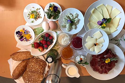 Kosz śniadaniowy ze świeżymi organicznymi jagodami, masłem ziołowym, twarogiem ziołowym, koktajlem ziołowym, jadalnymi kwiatami i świeżymi ziołami. 