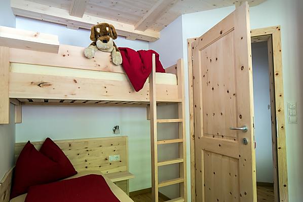 Zimmer in Zirmholz mit zwei Einzelbetten und einem Hochbett sowie direktem Zugang zum Badezimmer.