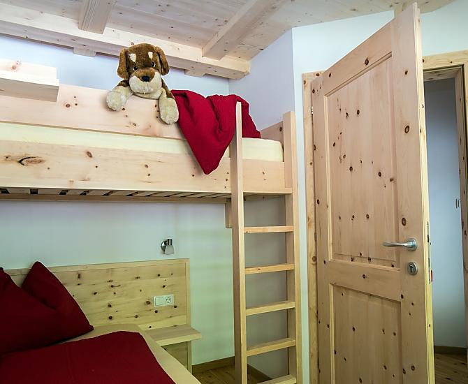 Zimmer in Zirmholz mit zwei Einzelbetten und einem Hochbett sowie direktem Zugang zum Badezimmer.