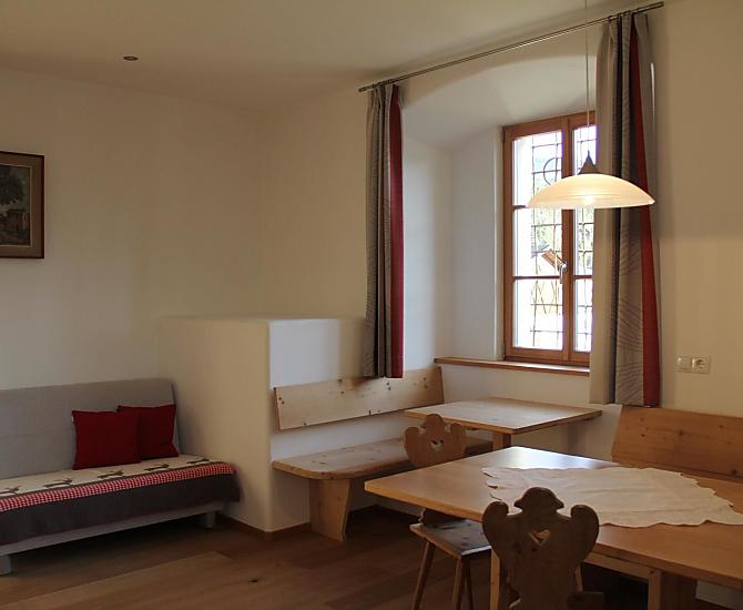 Geräumiger Wohnbereich mit Sofa, Ofen, Nische zum Sitzen sowie Tisch mit Eckbank.