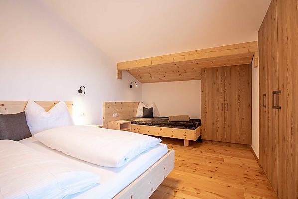  Schlafzimmer mit Doppelbett in Zirbenholz und direktem Zugang zum Balkon.